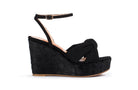 A single black wedge sandal with an ankle strap and a knotted front detail, shown in profile against a plain white background.